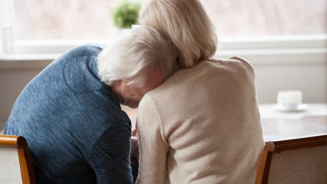 Bildet viser et eldre par som sitter inntil et bord. Mannen lener hodet sitt på kvinnens skulder.