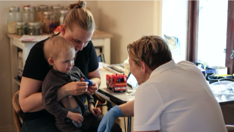 Bildet viser barnesykepleier Nina Granum Lycke på jobb. Her snakker hun med en liten syk gutt som sitter på fanget til sin mor.