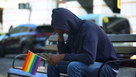 Bildet viser et ungt menneske med hodet bøyd. Vedkommende har pride-flagget i hånden.