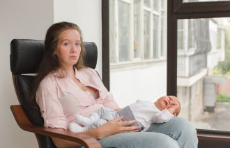 Bildet viser en nedstemt mor som sitter med babyen liggende på fanget