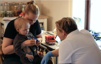 Bildet viser barnesykepleier Nina Granum Lycke på jobb. Her snakker hun med en liten syk gutt som sitter på fanget til sin mor.