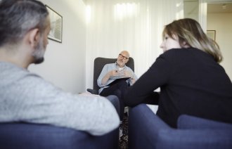 Bildet viser en mannlig terapeut som er vendt mot leseren. Foran ham sitter en mann og ei dame, som vi ser ryggen på.