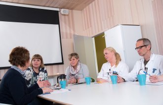 Bildet viser helsepersonell som sitter rundt et bord og snakker sammen. Noen har sykepleieruniform på seg, mens andre har vanlige klær.