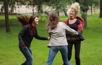 Tre kvinner danser i ring ute i en park