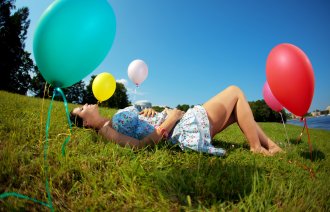 Bildet viser en gravid kvinne liggende i en eng med ballonger rundt omkring.