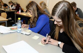 Bildet viser to kvinnelige studenter som sitter ved pultene på Universitetet i Agder