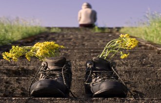 Bildet viser et menneske som sitter med ryggen til øverst i en trapp ute i det fri. Det står et par sko for seg selv på trappen med blomster i.