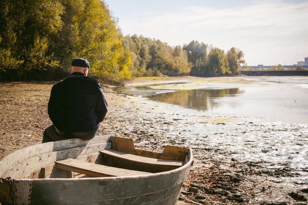 Bildet viser en mann som sitter på en båt og ser ut over en innsjø