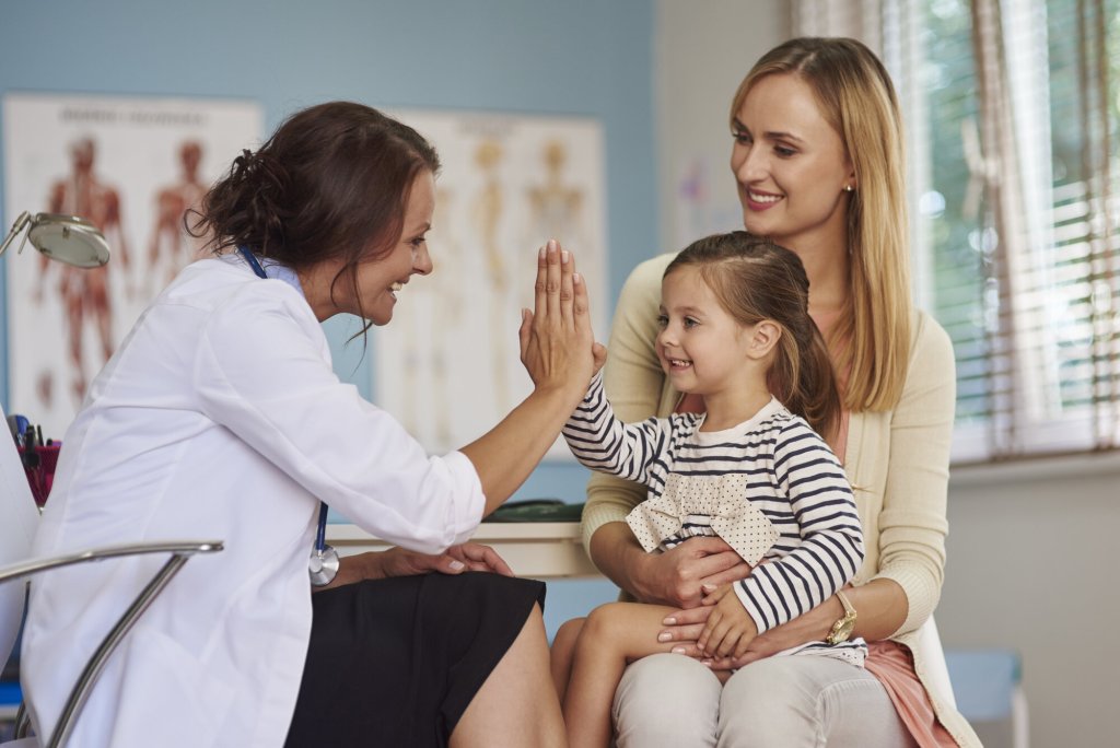 Bildet viser en liten datter på fanget til mora. Dattera gjør high five med en helsesykepleier som sitter overfor dem