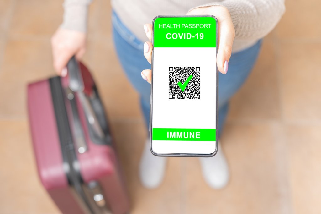 Bildet viser en kvinne med en koffert som viser, med mobilen sin, at hun er vaksinert for covid-19