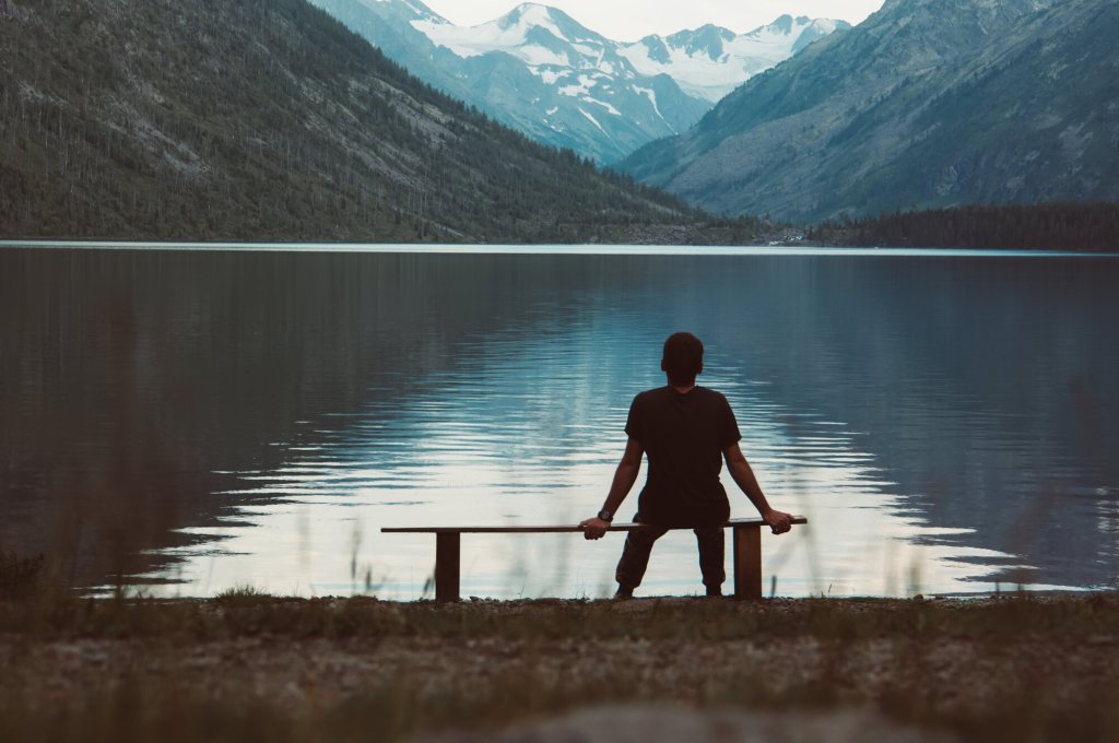 Bildet viser en mann som sitter alene på en benk og ser utover fjorden