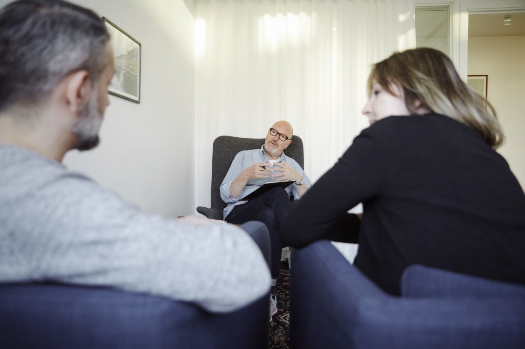 Bildet viser en mannlig terapeut som er vendt mot leseren. Foran ham sitter en mann og ei dame, som vi ser ryggen på.