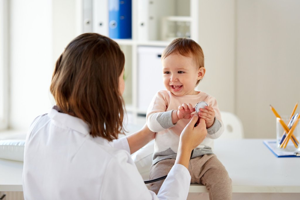 En blid baby sitter på et bord og blir undersøkt av en helsearbeider.