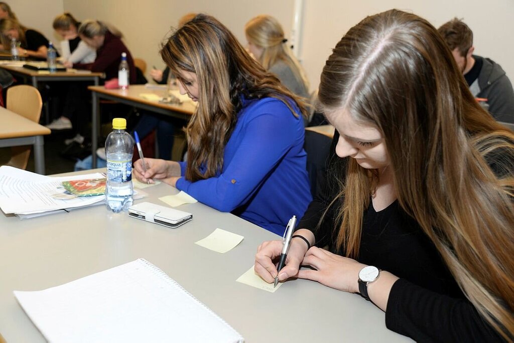 Bildet viser to kvinnelige studenter som sitter ved pultene på Universitetet i Agder