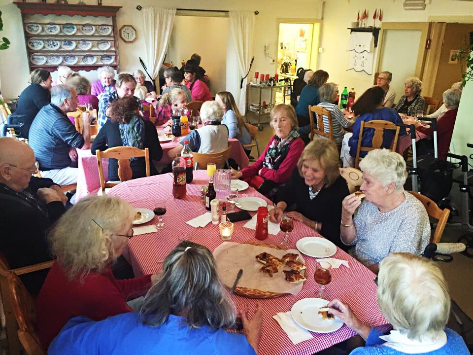 Folk sitter rundt bord og spiser pizza og har quiz. 