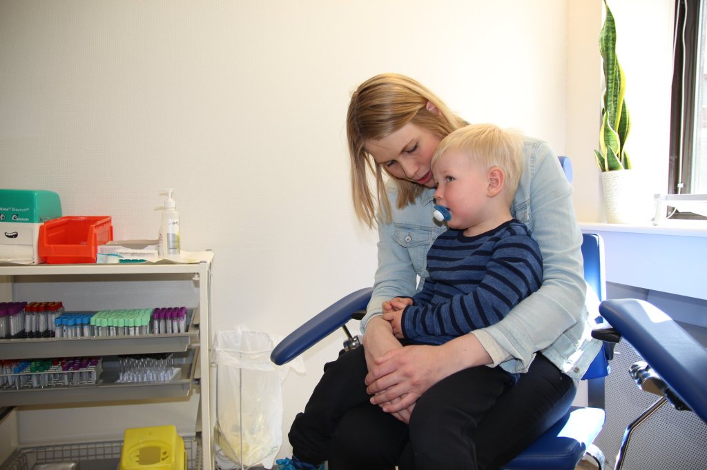 Sebastian sitter på mammas fang og venter på blodprøve.