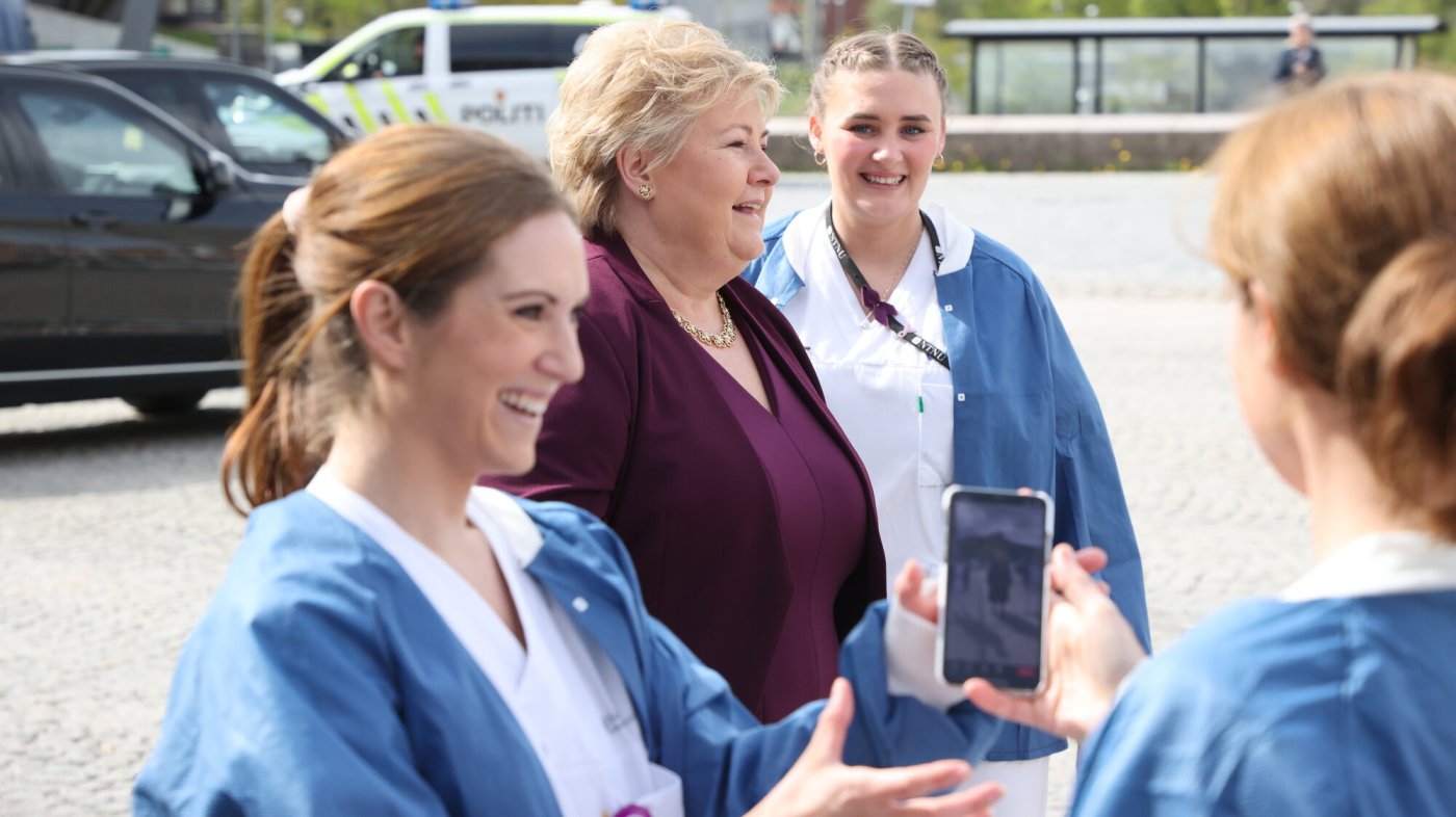 Bildet viser Ida Gerø med mobiltelefon, i bakgrunnen statsminister Erna Solberg og andre sykepleiere.