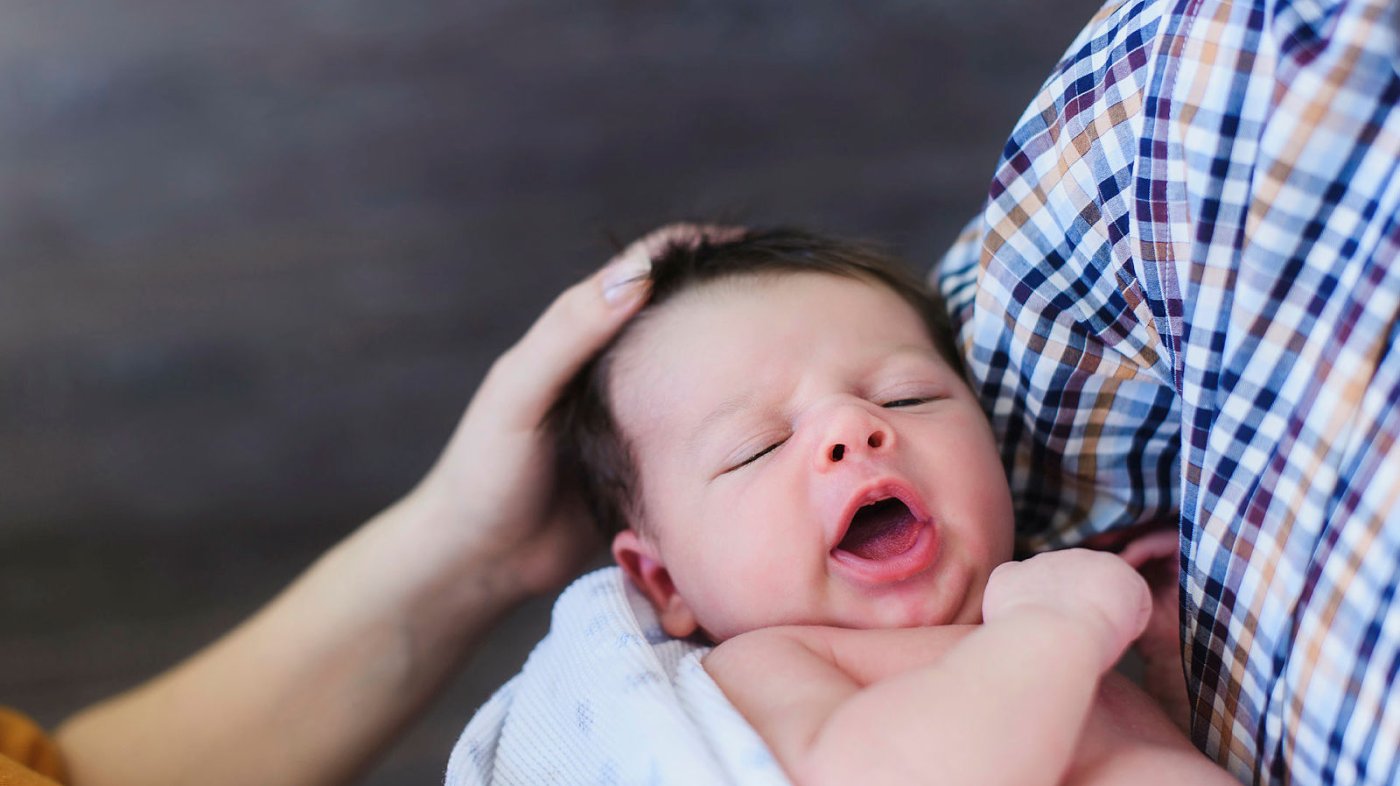 Liten baby som gjesper mens han/hun får kos av mor og far.