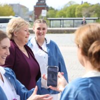 Bildet viser Ida Gerø med mobiltelefon, i bakgrunnen statsminister Erna Solberg og andre sykepleiere.