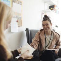 Bildet viser en smilende, kvinnelig helsesykepleier i samtale med en annen kvinne.